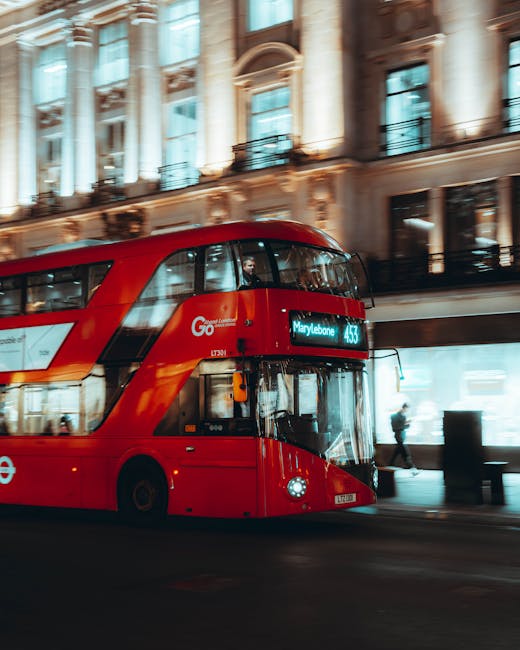 A red double-decker London bus traveling along a city street during daytime, with a digital route display showing 'Marylebone' and the route number '43'. The bus is modern with a sleek, shiny exterior, and large tinted windows that reflect nearby building facades. In the background, there is an ornate, historic building with tall columns, decorative stonework, and balconies featuring black wrought-iron railings. Pedestrians are visible walking on the sidewalk, some partially obscured by the bus. The street scene is illuminated by natural daylight, highlighting the vibrant red of the bus against the neutral tones of the historic architecture and the pavement, illustrating urban public transport close to private waste management services in a central London environment. Rubbish removal specialists like Rubbish Removal Marylebone work within such busy areas, often managing waste generated in commercial and residential properties that remain accessible despite high-traffic surroundings.